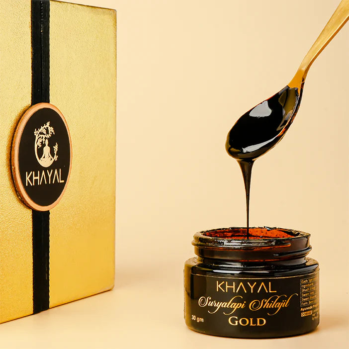 A spoon drizzles thick, dark syrup into an open jar labeled KHAYAL Swarnapatri Shilajit GOLD beside a gold-colored box with a KHAYAL logo, set against a light beige background.